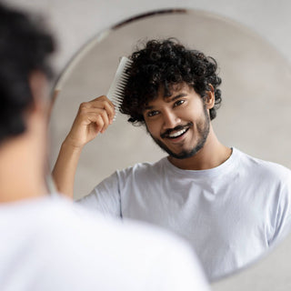 Jonge man lacht in de spiegel terwijl hij met z'n haarzerzorging bezig is.