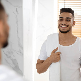 Jonge man lachend in de badkamerpiegel terwijl hij bezig is met het reinigen van zijn lichaam.